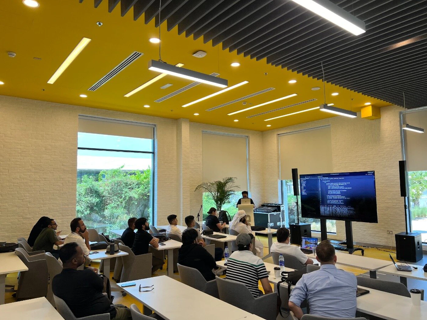 (Photo) A photo of a group of people in a modern conference room, attending a presentation displayed on a large screen. people | indoor | presentation, conference room | candid Note: The image is a real-life captured scene of a presentation in a conference room, making it a photograph.