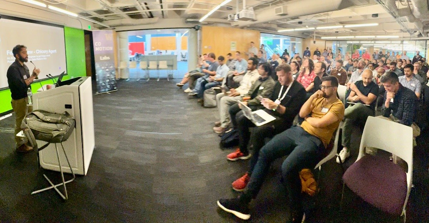 (Photo) A man is giving a presentation to a large audience sitting in rows of chairs. Text: Fei Xia • Chicory Agent people | indoor | presentation, audience, speaker | candid Note: The image is a real-life capture of an event, showing a presenter and an audience. This clearly falls under the category of a photograph.