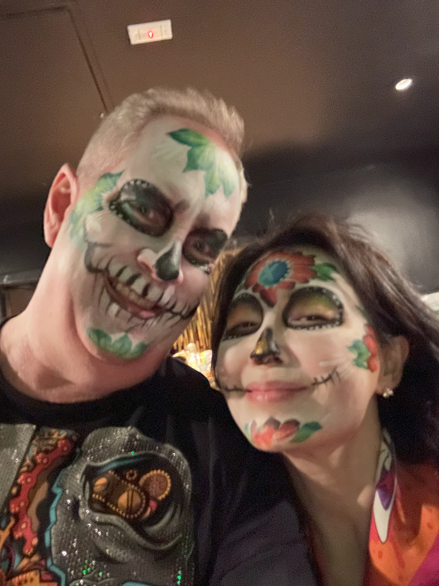 (Photo) A selfie of two people with Dia de los Muertos face paint. person | indoor | Two people, face paint, Dia de los Muertos theme | selfie Note: The image is a real-life photograph capturing a moment with two individuals. It is not a drawing, logo, or banner.