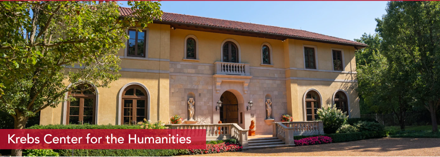(Photo) The image displays a large, ornate building with a light yellow facade, a red-tiled roof, and arched windows, surrounded by lush green trees and landscaping under a clear blue sky. A red banner at the bottom of the image identifies the building as the 'Krebs Center for the Humanities'. Text: Krebs Center for the Humanities building, architecture, landscape | outdoor, daytime | Mediterranean/Italianate architectural style, stone facade, arched windows, statues flanking the entrance, lush green trees and shrubs, red banner with text. | architectural photography, informational | Colors: #E8D3A8, #D4C09B, #8B0000, #5F8B33, #6B9FD8 Note: This image is categorized as a 'photo' because it is a realistic photographic capture of a physical building and its surroundings. The text overlay serves as an informational caption for the photograph rather than being the primary visual element.