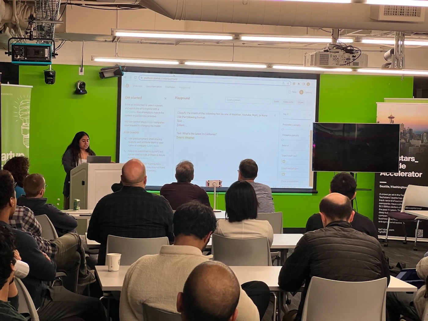 (Photo) A woman is presenting to a group of people in a room with a green wall.  A projected screen displays a web page and there is a second screen visible. Text: Get started Playground Classify the items of the following list: Pen, Riddle, Hulk, or None Save Test What's the brand's mascot? Ethan Nestor Frequency category Level of formality 1000 Gen stars_ Accelerator Seattle, Washington A crown jewel of the Techstars Castle has completed another successful year. Since 2015, the Techstars Seattle accelerator has seen $1.2 Billion dollars of company exits and 90% of companies are still active. people | indoor | presentation, audience, projector screen | candid Note: The image is a real-life captured scene of a presentation, making it a photograph.  It's not staged or posed for artistic purposes.