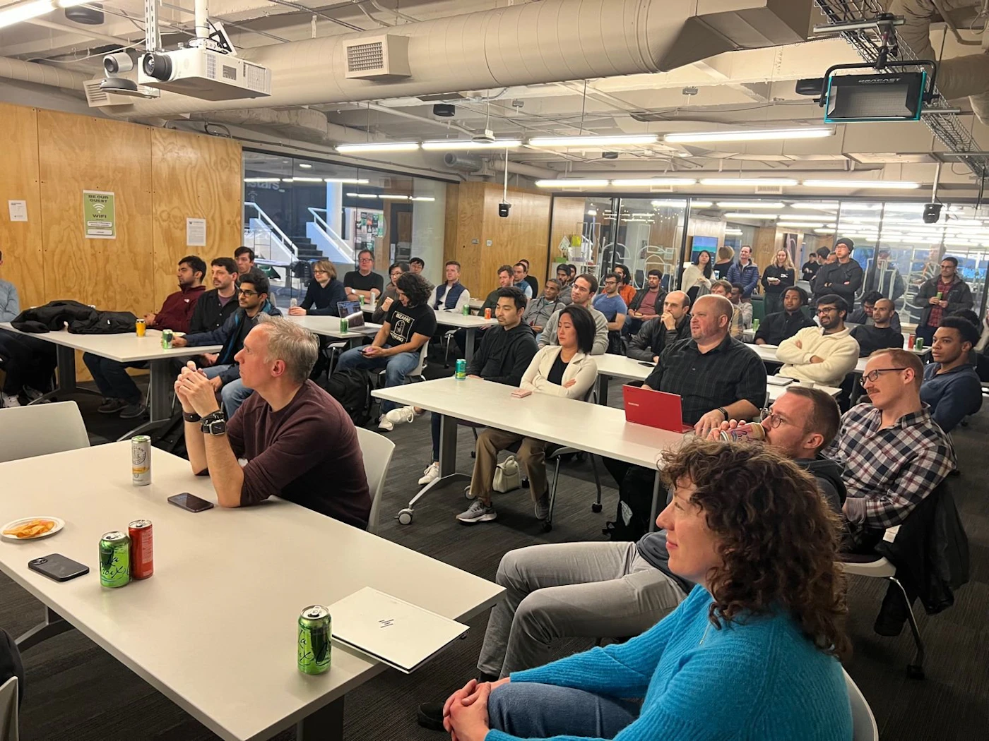 (Photo) A photo of a group of people sitting at tables in a room, appearing to be attending a presentation or meeting. people | indoor | group of people, presentation setting, tables and chairs | candid Note: The image is a real-life captured image of a scene with people in a room, making it a photograph.  It's not a logo, illustration, banner, or handwriting.