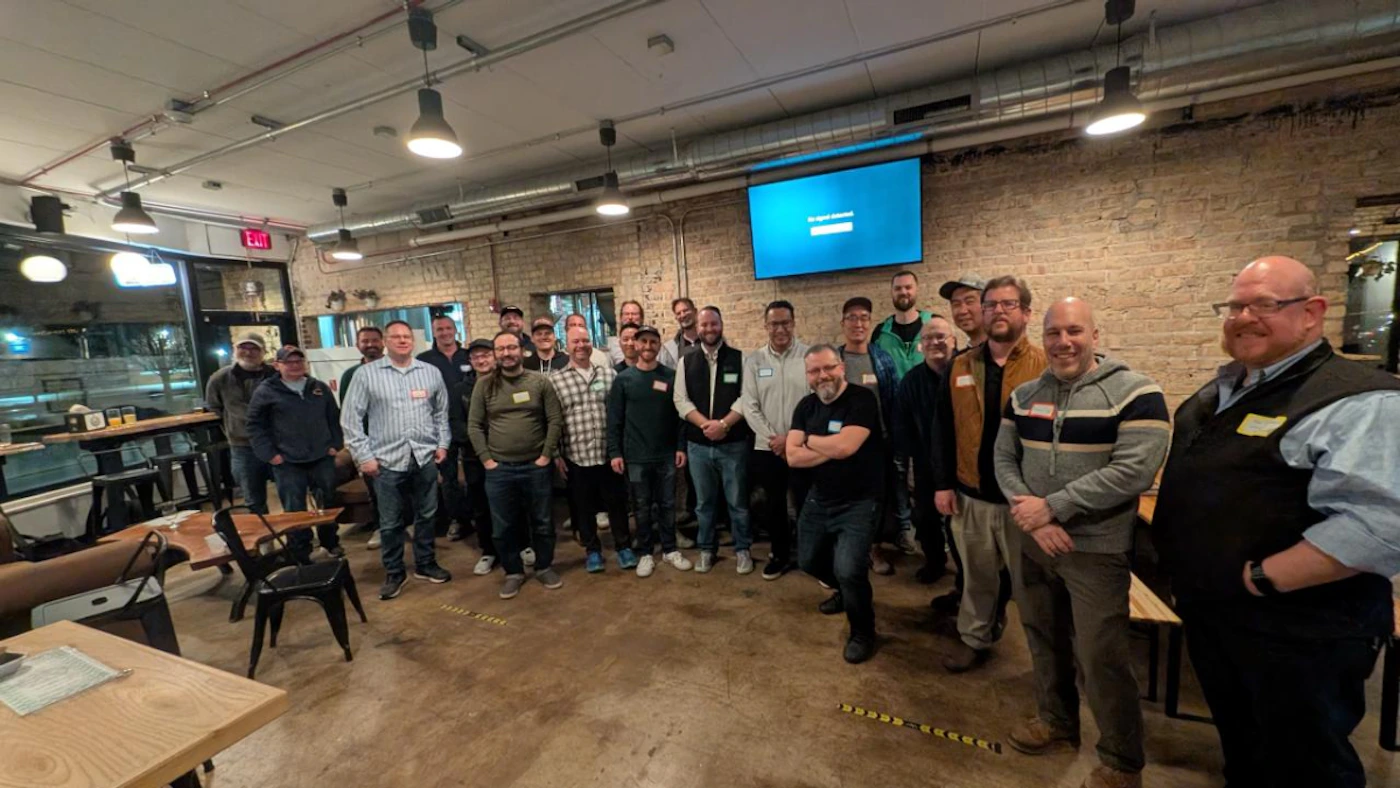 (Photo) A group of adult men are gathered indoors, likely in a restaurant or event space, posing for a photograph. Many of them are wearing name tags, and a large screen displaying 'No signal input' is visible on the brick wall in the background. Text: No signal input EXIT A group of adult men | Indoor, appears to be a casual gathering space like a restaurant or bar with exposed brick walls and industrial-style lighting. | Multiple people (approximately 30), most are smiling and looking towards the camera, many wearing name tags, a large blue screen, and industrial-style interior design elements. | Group portrait, candid, wide shot. | Colors: #8B664B, #007bff, #4F4F4F, #A9A9A9 Note: The image captures a real-world scene with multiple people and objects in a specific setting, which is characteristic of a photograph.