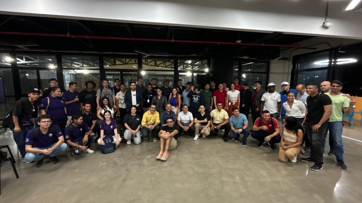 This is a photo of a large group of people posing together in what appears to be an office or event space. They are standing and crouching, looking towards the camera.