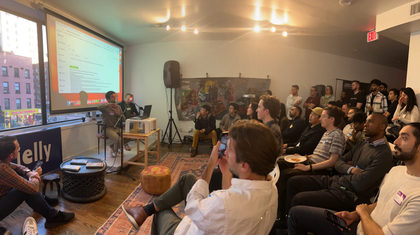 (Photo) A group of people are sitting and watching a presentation being given by a person standing near a projector screen. Text: Jelly people | indoor | presentation, audience, projector screen | candid Note: The image is a real-life captured scene of an event, depicting people and their environment, making it a photograph.