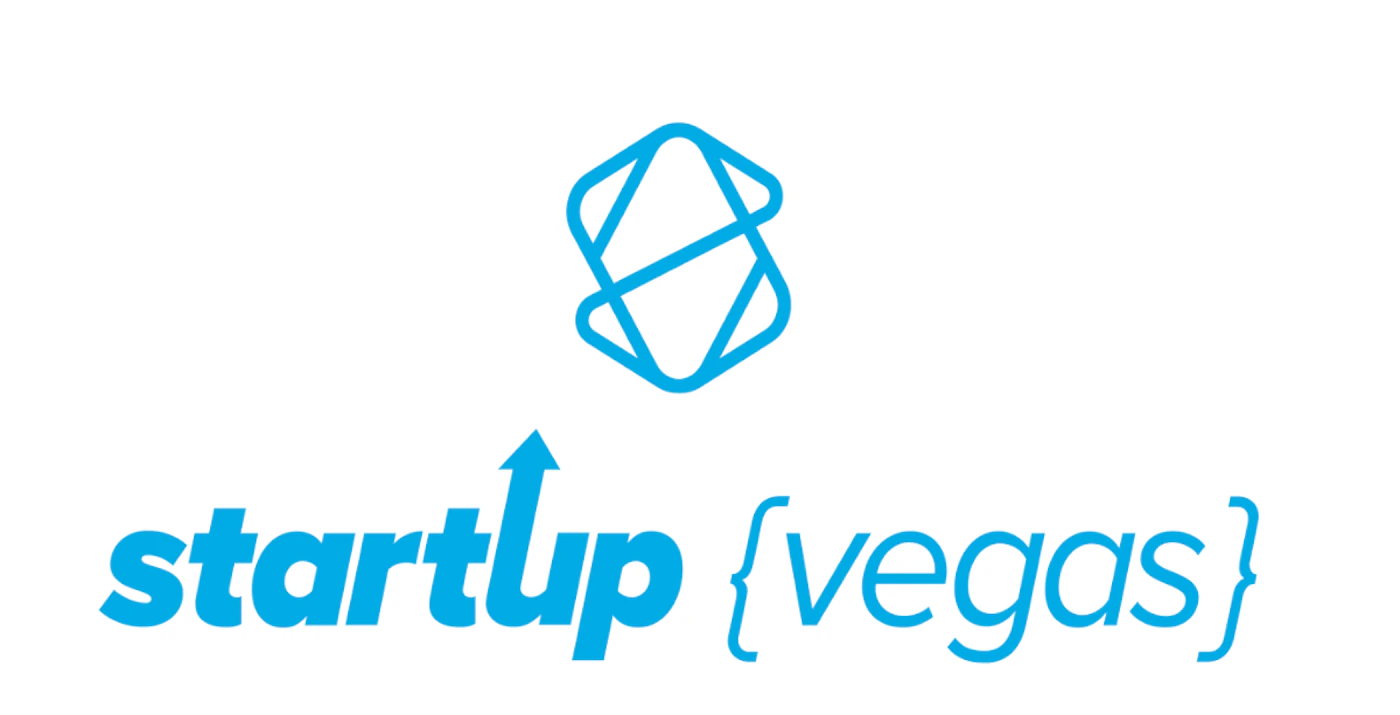 (Logo) A logo featuring a bright blue abstract geometric symbol above the stylized text 'startup {vegas}'. The 'u' in 'startup' has an upward-pointing arrow. Text: startup {vegas} Colors: #00AEEF Note: The image clearly serves as a brand identifier, combining a unique graphic symbol with stylized text. Its clean design and singular focus on representing an entity classify it as a logo.