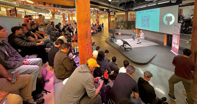 (Photo) A photo of an audience watching a presentation in a large, modern space. Two presenters are on a stage in front of a large screen displaying a QR code and a logo. Text: #Auth0USERS - SAN FRANCISCO people | indoor | presentation, audience, stage, screen | candid Note: The image is a real-life capture of an event, depicting people and a presentation setting.  It's not a drawing, logo, or banner itself.