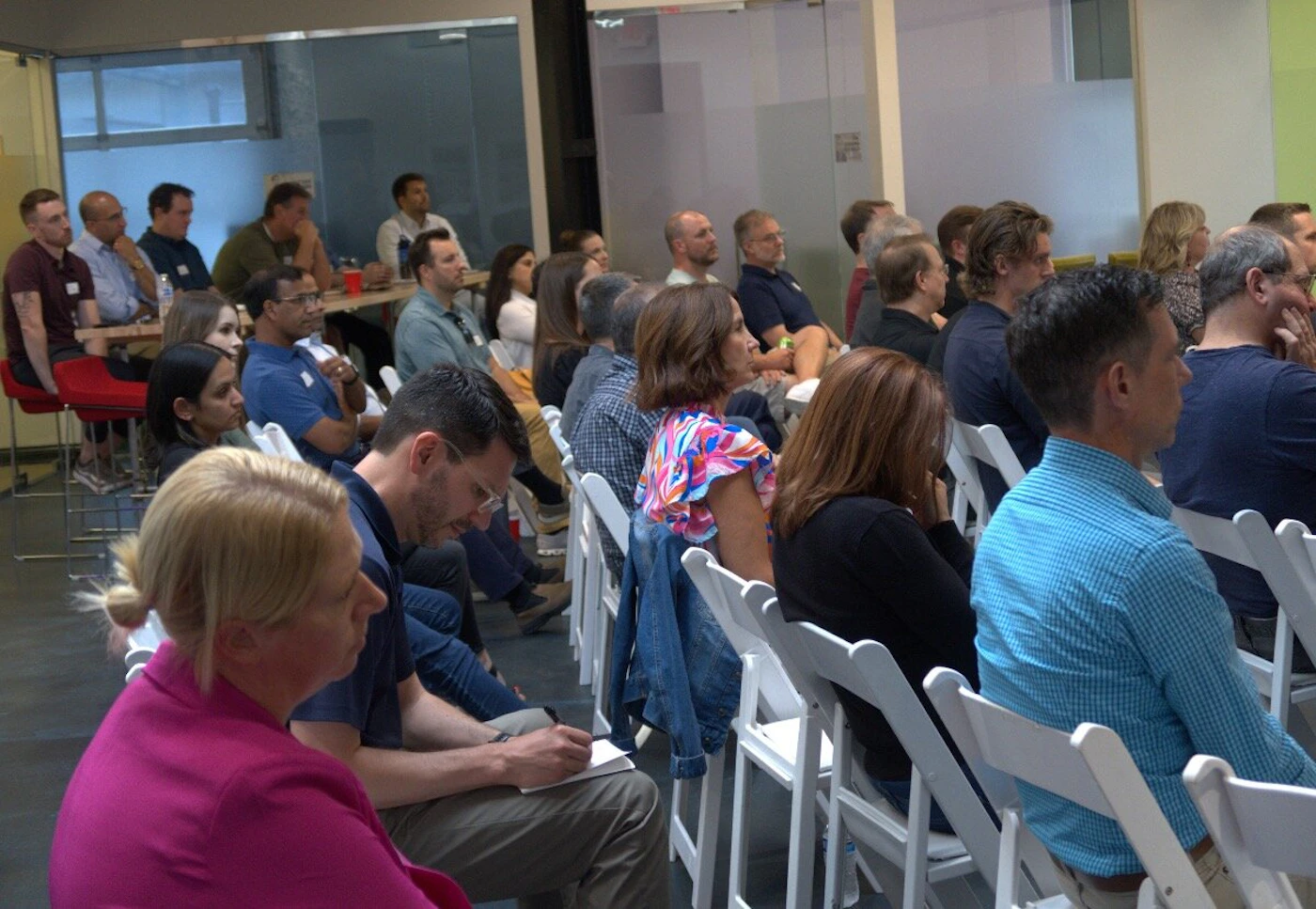 (Photo) The image shows a group of people sitting in chairs, seemingly attending a presentation or meeting. The setting appears to be an office or event space. group of people | indoor | multiple people, chairs | candid | Colors: #A9A9A9, #FFFFFF, #000080, #D2691E Note: The image depicts a real-life scene with people and objects, indicating it's a photograph rather than an illustration or other type of image.