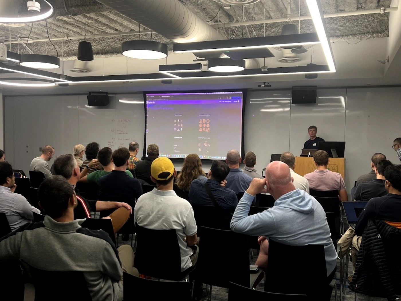 (Photo) A group of people are sitting in chairs in a presentation room, watching a presentation on a large screen. people | indoor | presentation, audience, screen | candid Note: The image is a real-life captured image of a scene, depicting a presentation setting.  This clearly falls under the category of a photograph.