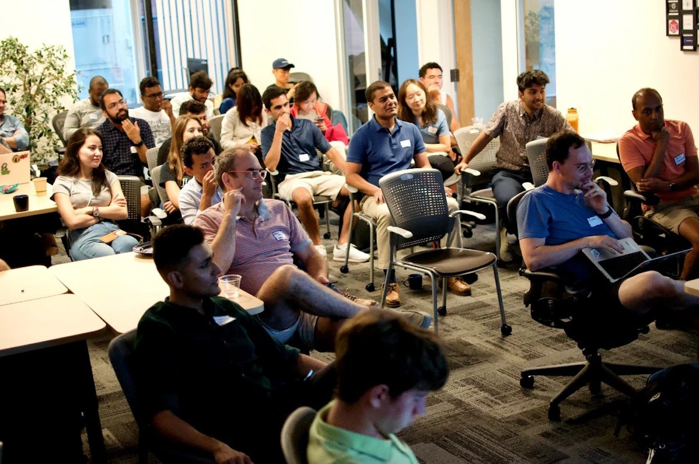 (Photo) A photo of a group of people sitting in chairs in a room, appearing to be attending a presentation or meeting. people | indoor | group of people, meeting room | candid Note: The image is a real-life captured image of a group of people in a meeting room setting.  It exhibits characteristics of a candid photograph.