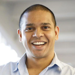 (Photo) A headshot of a smiling man with short hair, wearing a light blue collared shirt. person | indoor | headshot, smiling | portrait Note: The image is a real-life captured image of a person, making it a photograph. It's a posed headshot, likely for a professional profile.