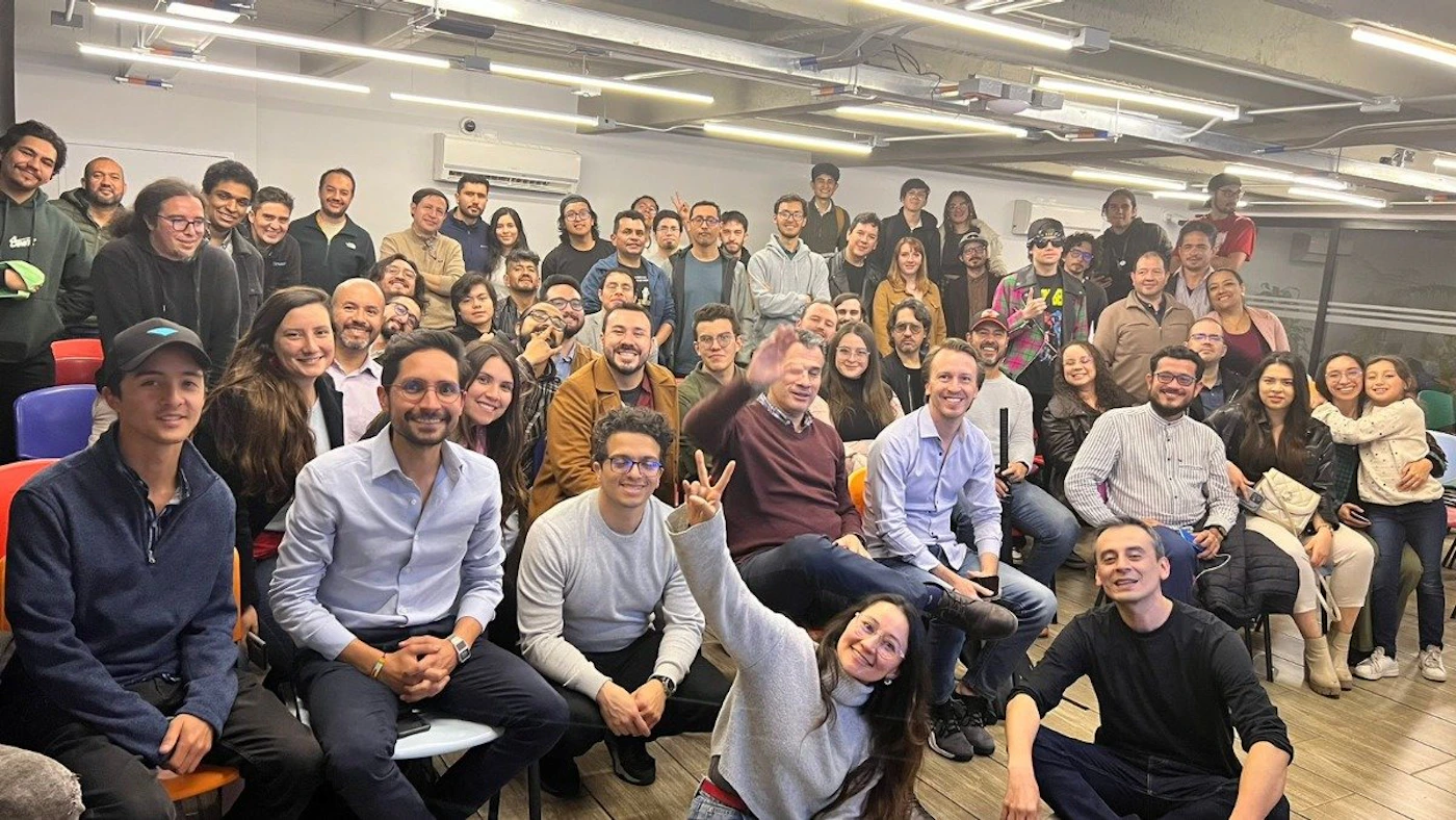 (Photo) A large group of people is posing for a photo indoors. They are sitting and standing in rows, smiling at the camera. people | indoor | large group | group photo Note: The image is a real-life captured moment of a group of people, indicating it's a photograph. It's not a logo, illustration, banner, or handwriting.