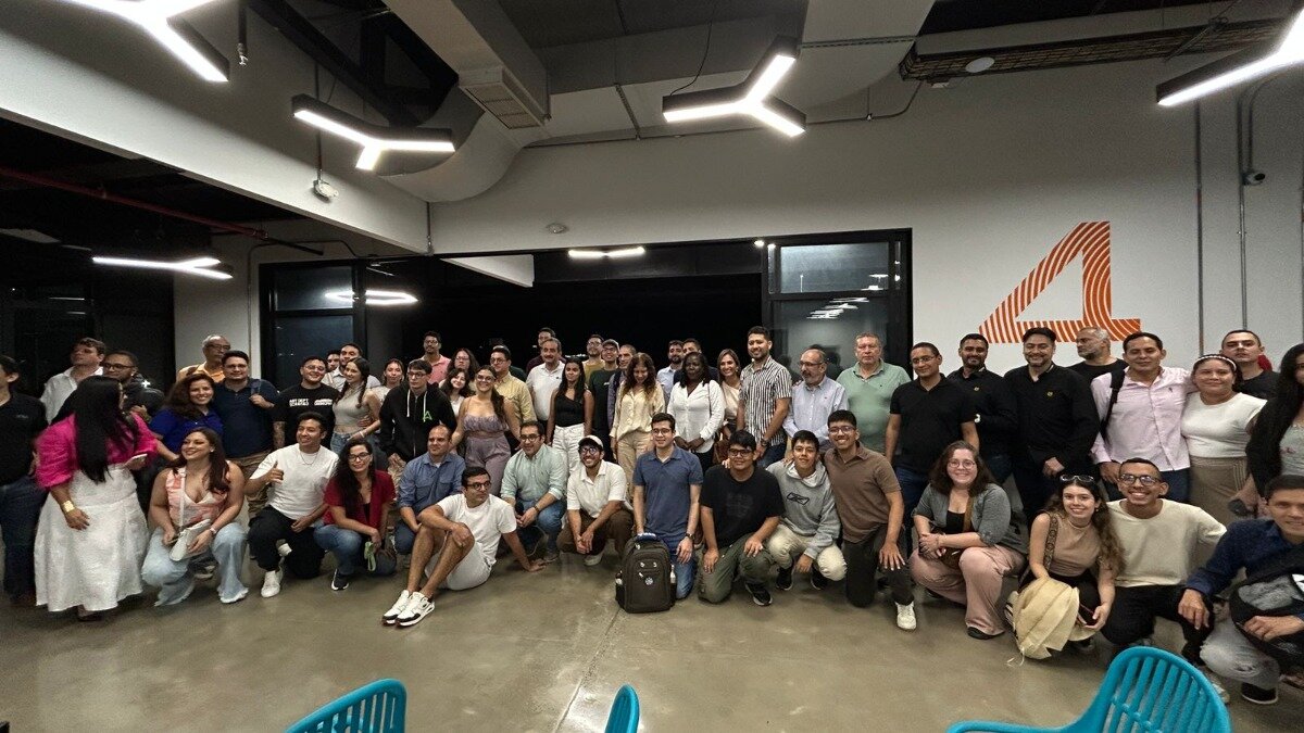 A large group of people, appearing to be colleagues or participants in an event, are posing for a photograph indoors. Some individuals are standing while others are crouching in the front row, all looking towards the camera.. Text: 4