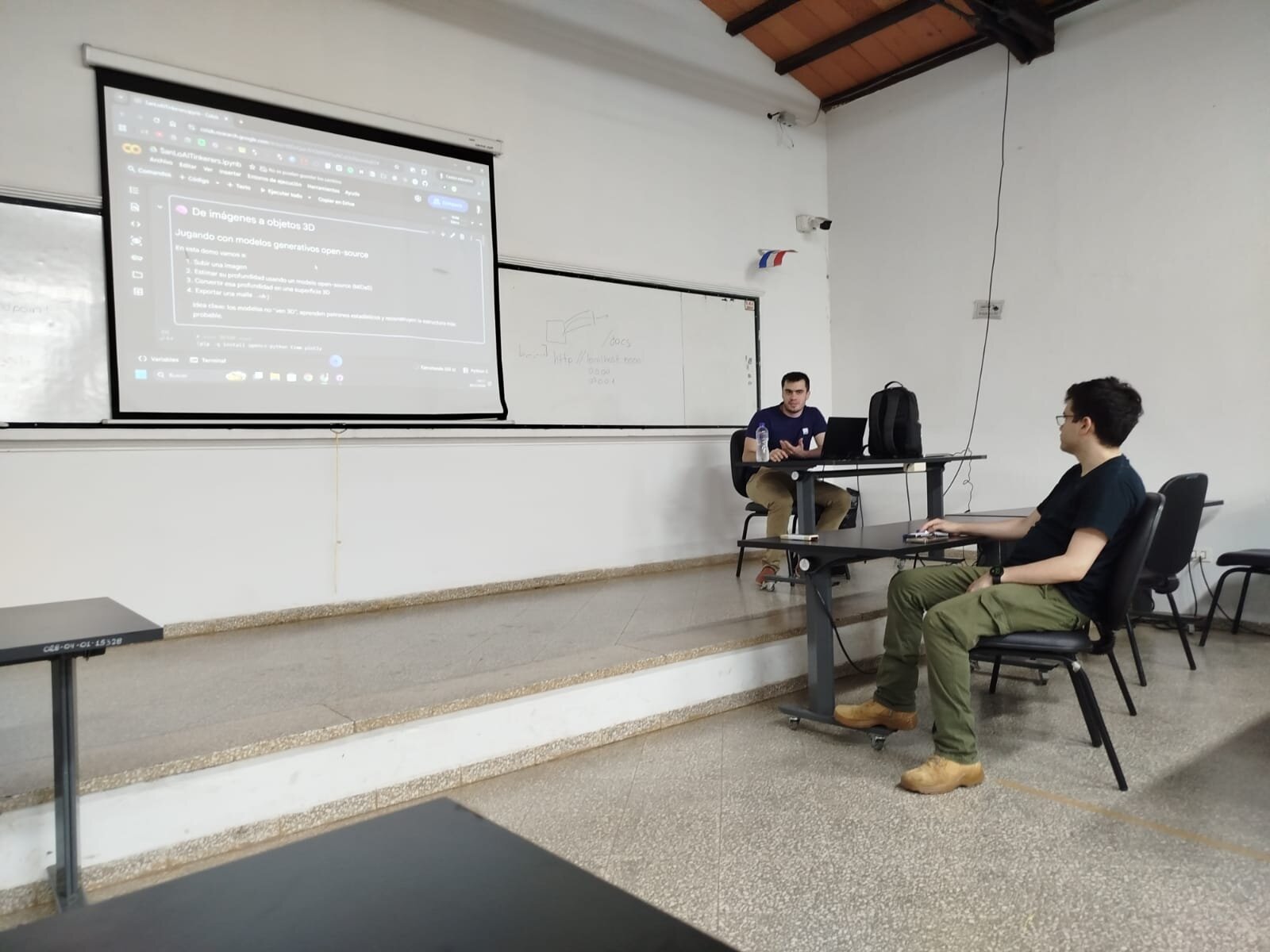 (Photo) A man is giving a presentation in a classroom, with a projector screen showing a Google Colab notebook in Spanish about 3D object generation. Text: De imágenes a objetos 3D Jugando con modelos generativos open-source En esta demo vamos a: 1. Subir una imagen 2. Estimar su profundidad usando un modelo open-source (MiDaS) 3. Combinar esa profundidad en una superficie 3D 4. Exportar una malla (.obj) Para correr los modelos en Colab, primero debemos instalarlos y descargar los pesos de los modelos. /docs presentation | indoor | projector screen, whiteboard, laptops | candid | Colors: #FFFFFF, #D3D3D3, #808080 Note: The image is a real-life photograph capturing a scene in a classroom setting with people and physical objects.