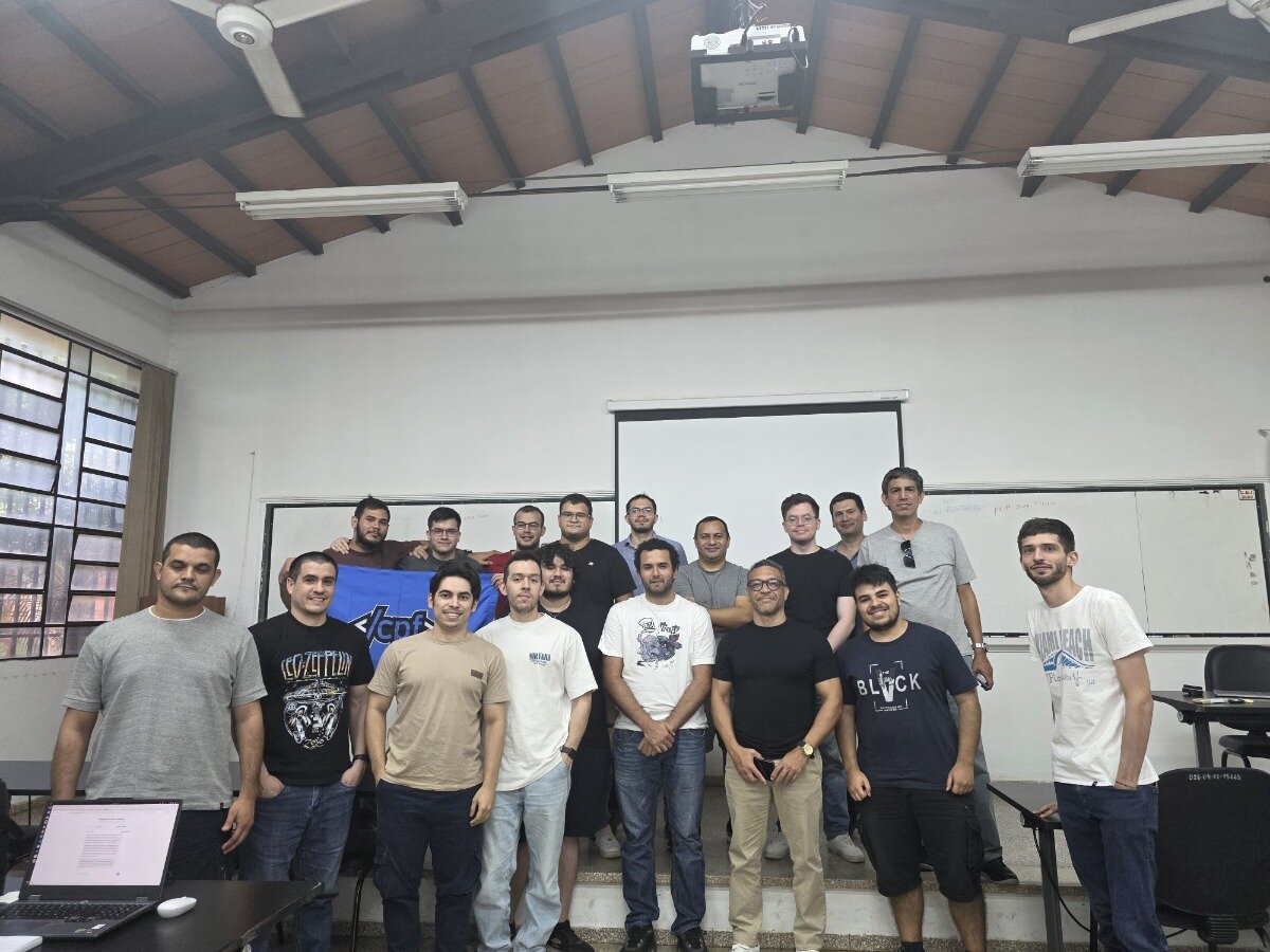 A group of eighteen men posing for a group photograph in a classroom or lecture hall, standing in front of a white projector screen and a whiteboard.. Text: </cpf> LED ZEPPELIN BLOCK SOUTH BEACH LAI