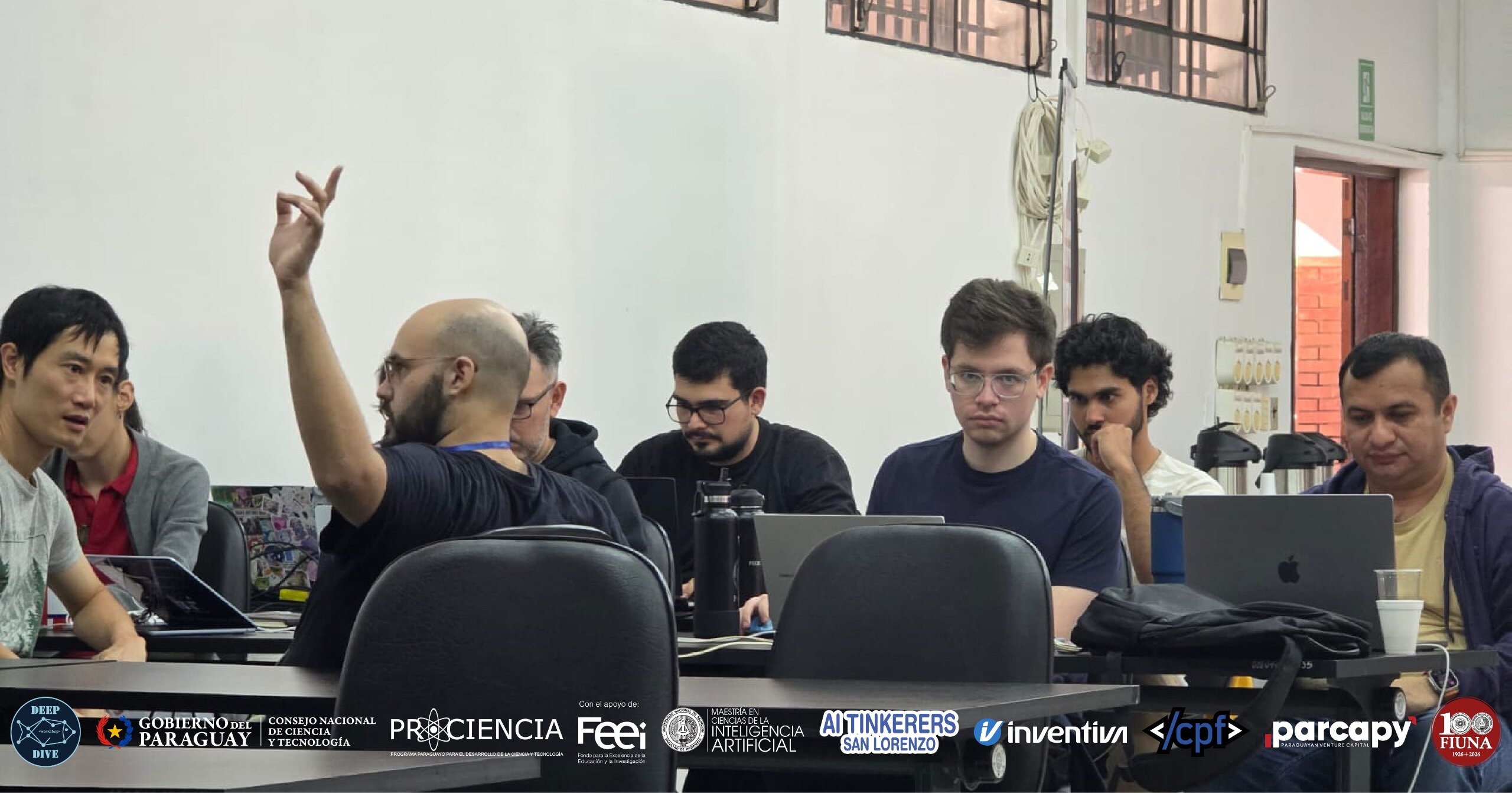 (Photo) A group of men are seated at a table with laptops in what appears to be a workshop or meeting, with one man raising his hand to speak. Text: DEEP DIVE GOBIERNO DEL PARAGUAY CONSEJO NACIONAL DE CIENCIA Y TECNOLOGÍA PROCIENCIA Con el apoyo de: Feei MAESTRÍA EN CIENCIAS DE LA INTELIGENCIA ARTIFICIAL AI TINKERERS SAN LORENZO inventiva </cpf> parcapy 100 FIUNA people in a workshop or meeting | indoor | hand raised, laptops, branding banner at the bottom | candid | Colors: #FFFFFF, #000000, #7D7D7D Note: The image is a real-life photograph capturing a group of people in an indoor setting, featuring natural lighting and realistic subjects.