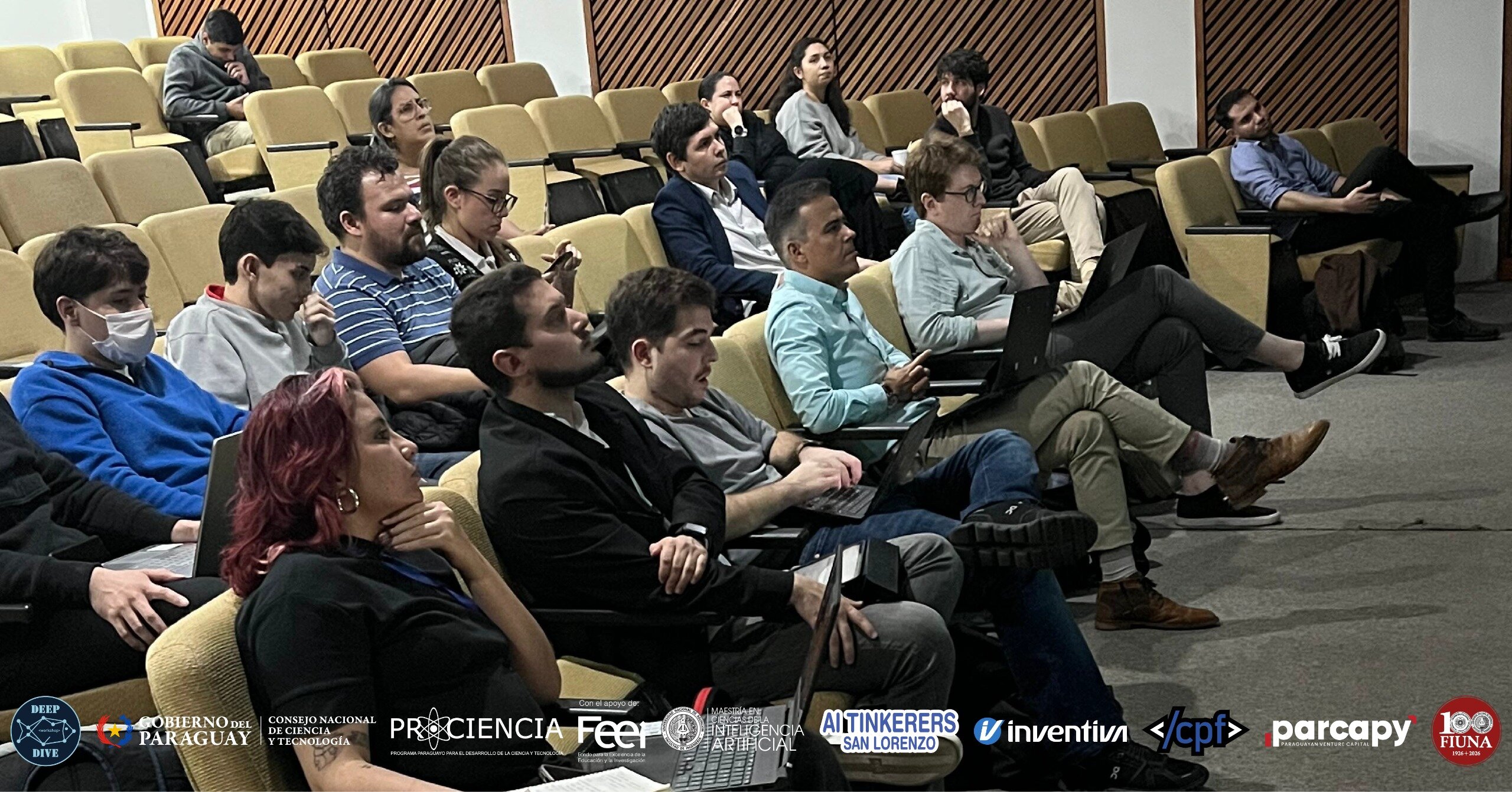 (Photo) An audience of young adults sits in a tiered auditorium, many with laptops open, focused on a presentation occurring off-camera. Text: DEEP DIVE, GOBIERNO DEL PARAGUAY, CONSEJO NACIONAL DE CIENCIA Y TECNOLOGÍA, PROCIENCIA, Con el apoyo de FEEI, MAESTRÍA EN INTELIGENCIA ARTIFICIAL, AI TINKERERS SAN LORENZO, inventiva, </cpf>, parcapy, 100 FIUNA people in an auditorium | indoor | tiered seating, laptops, audience members looking in one direction, banner of logos at the bottom | candid event photography | Colors: #d2b48c, #2b2b2b, #add8e6, #ffffff Note: The image is a real-life photograph of a group of people in an indoor setting.